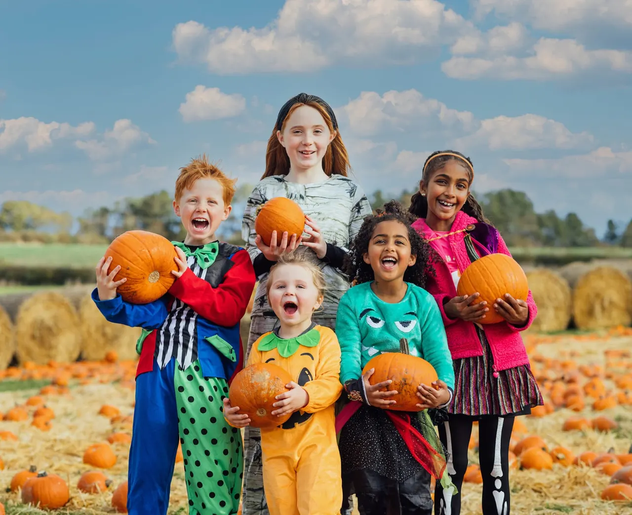Group of children holding pumpkins in a pumpkin patch field on a sunny day.