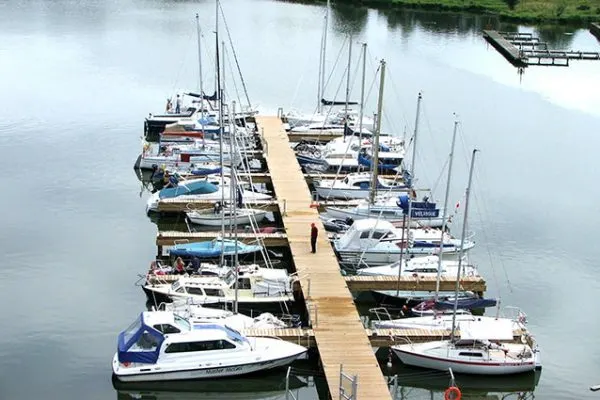 Moored sailboats and cabin cruisers lined up along a wooden jetty on calm water.