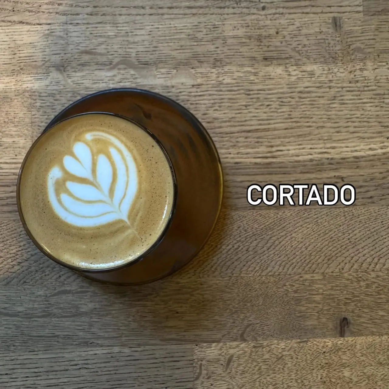 Cortado coffee with latte art in a dark cup on a wooden table.
