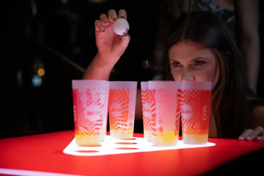 Child holding a glowing ball above illuminated cocktail glasses at a neon-lit interactive table.