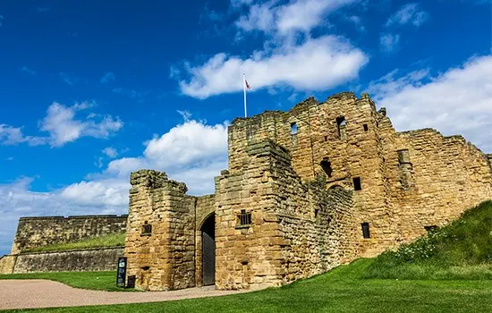 Stone castle ruins with crenellated towers and entrance archway on grassy hillside under blue sky.