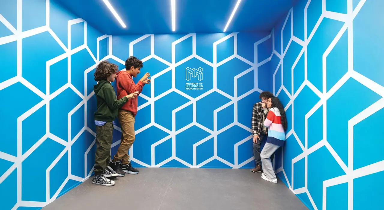 Children interact in a geometric blue and white illusion room with neon ceiling lights at a museum exhibition space.