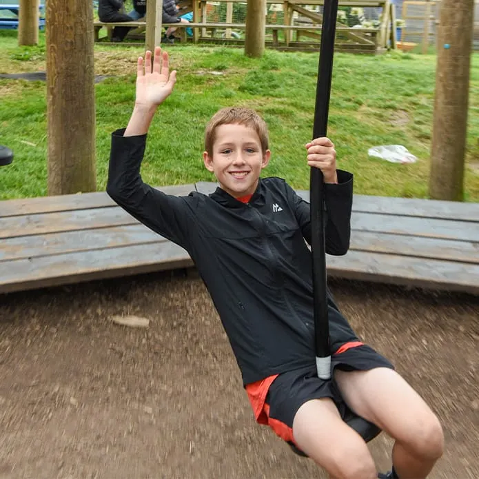 Child on a zip line suspended above a wooden platform at an outdoor play area.