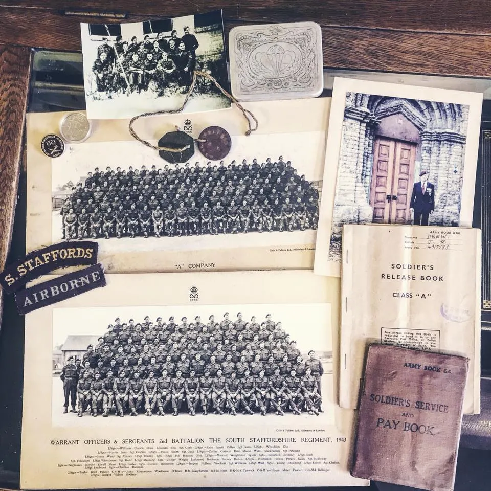 Collection of vintage military photographs, documents and memorabilia including regimental group portraits, soldier's release book, pay book and insignia displayed on wooden surface.
