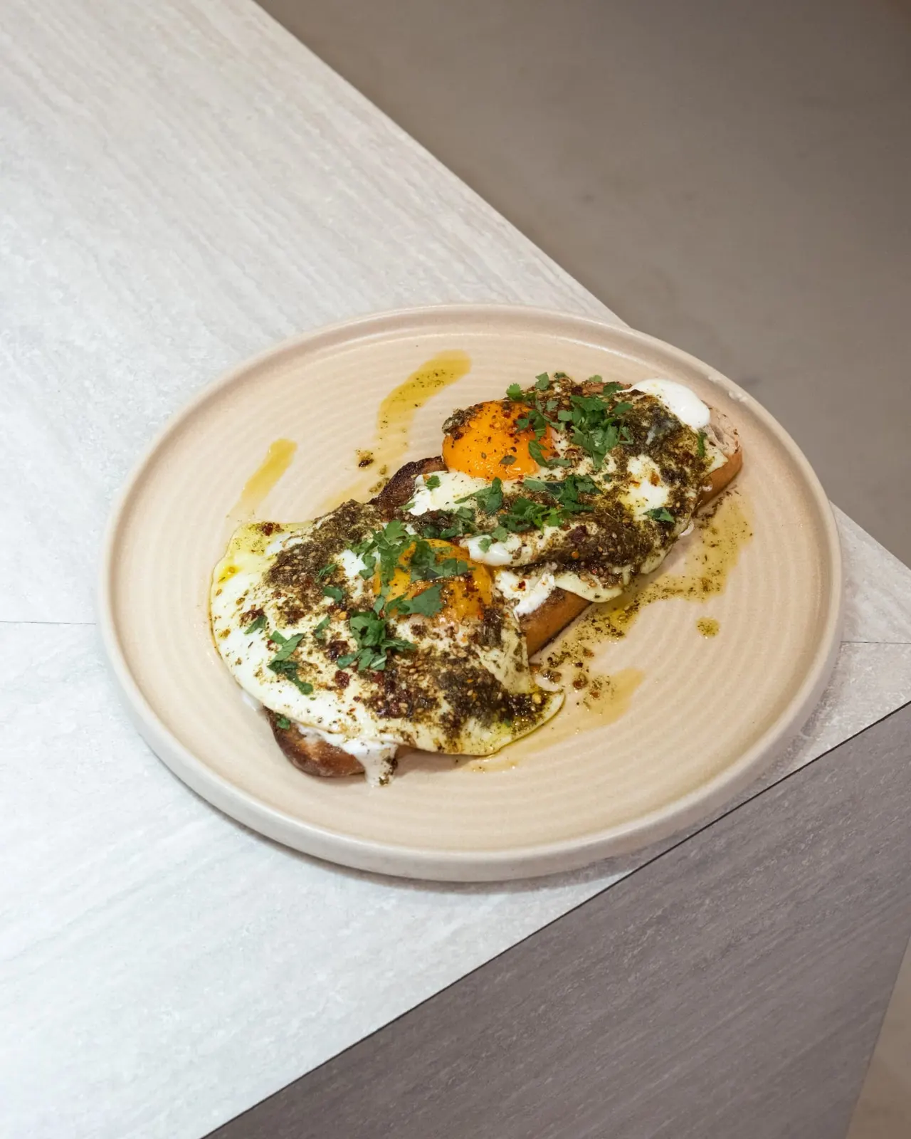 Toasted open sandwich topped with poached eggs, white cheese, za'atar seasoning and fresh herbs on a cream plate.