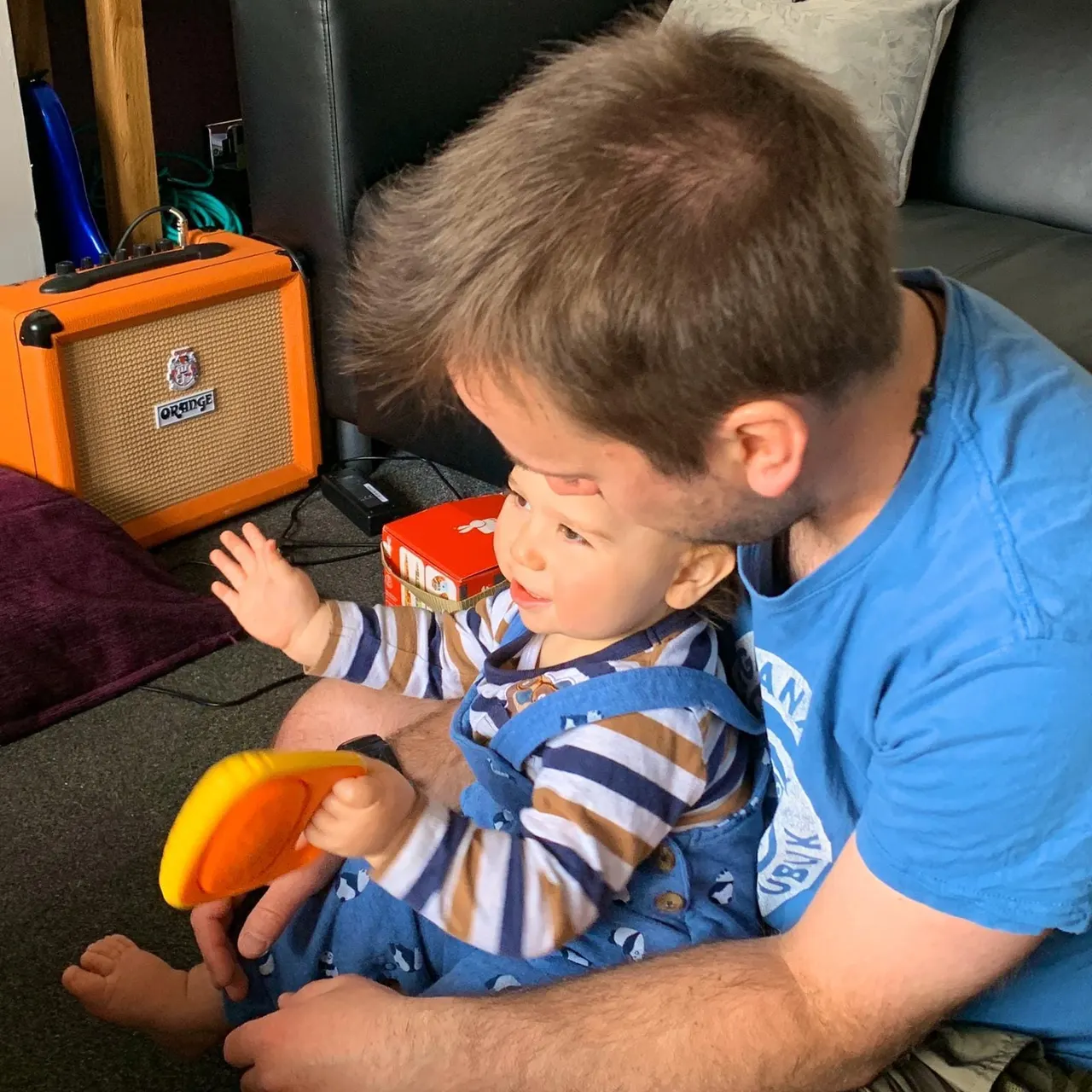 An adult and young child play with a toy together in an indoor music space with an orange amplifier.