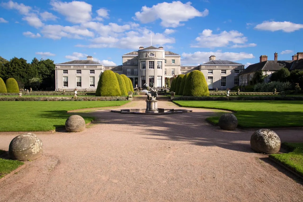 Formal gardens with gravel pathway leading to a grand neoclassical mansion, flanked by topiary hedges and a central fountain.