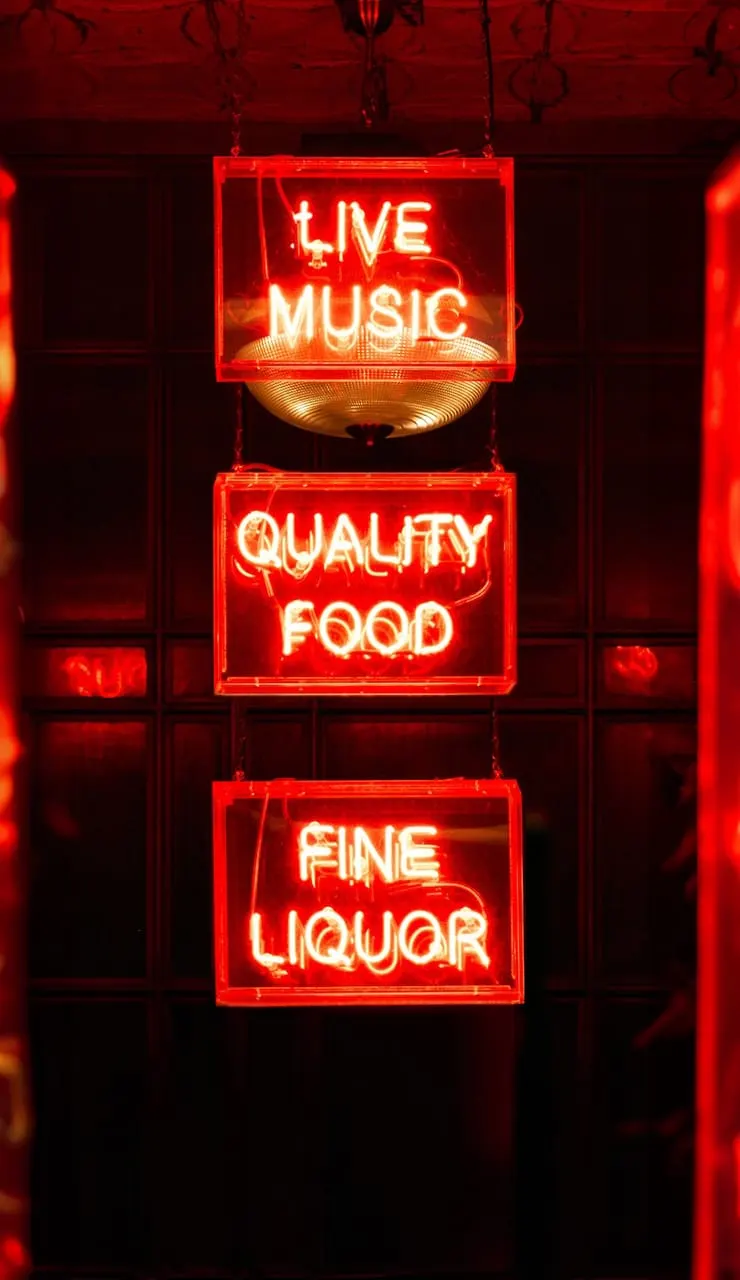Red neon signs advertising live music, quality food, and fine liquor hang in a darkened venue window.