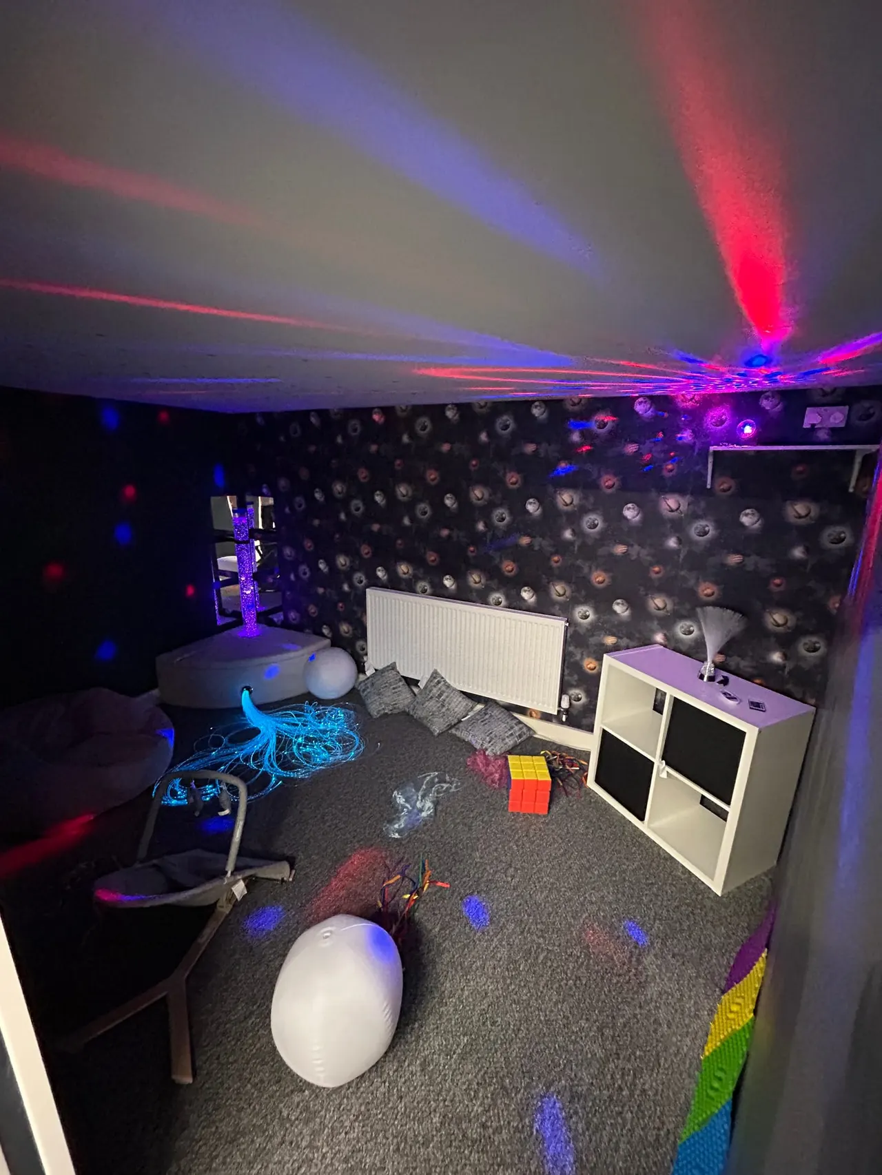 A soft play room with colourful laser lights, inflatable play equipment, storage cubbies and speakers on the walls.