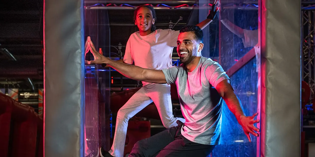 Two people enjoying an obstacle course challenge in a neon-lit indoor arena.
