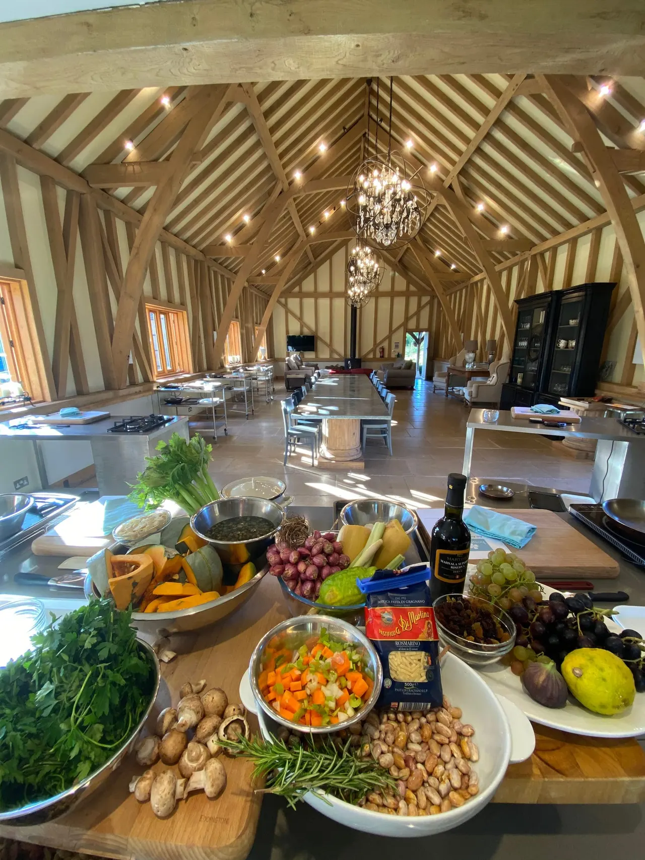 Food and ingredients laid out on a table inside a timber-framed barn with exposed beams and crystal chandeliers.