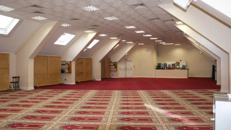 Large empty hall with red and cream patterned carpet, wooden storage cupboards and skylights in the ceiling.