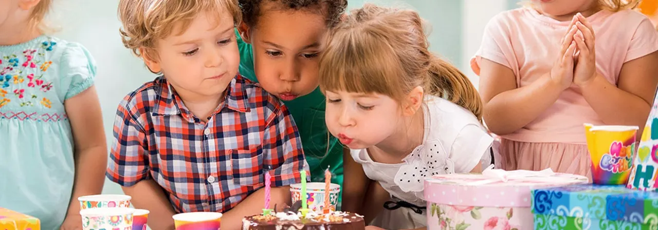 Young children gathered around a birthday cake with candles during an indoor party celebration.