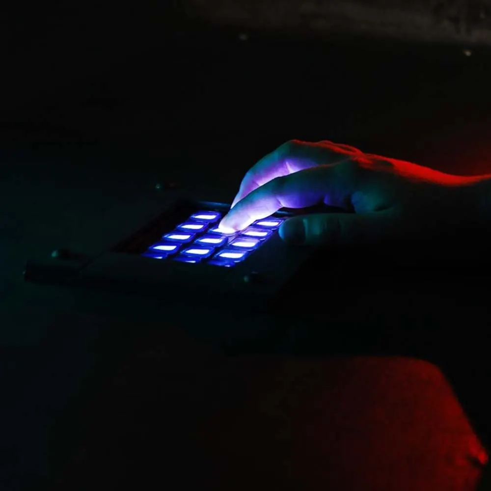 Hands operating an illuminated blue button pad in darkness with coloured lighting effects.