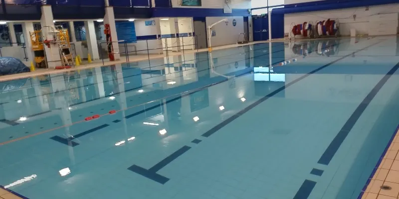 Empty indoor swimming pool with lane dividers and blue water, viewed from poolside.