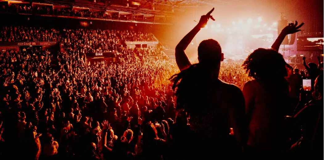 Packed concert crowd facing a brightly lit stage at the arena.