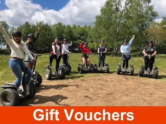 A group of people on Segways in a grassy outdoor area, some with arms raised, trees in background.