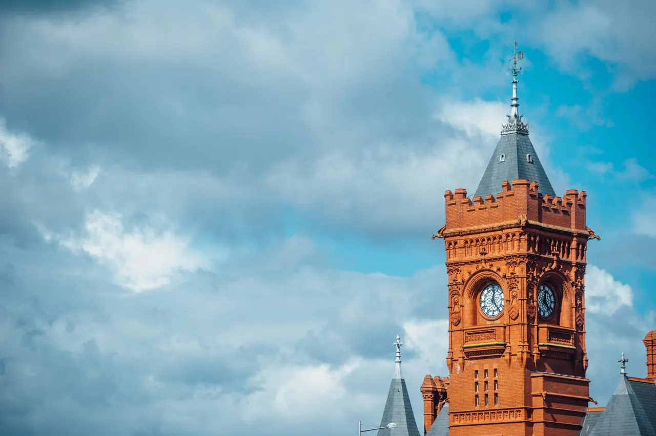 Red brick Victorian clock tower with ornate turrets against a bright blue cloudy sky.