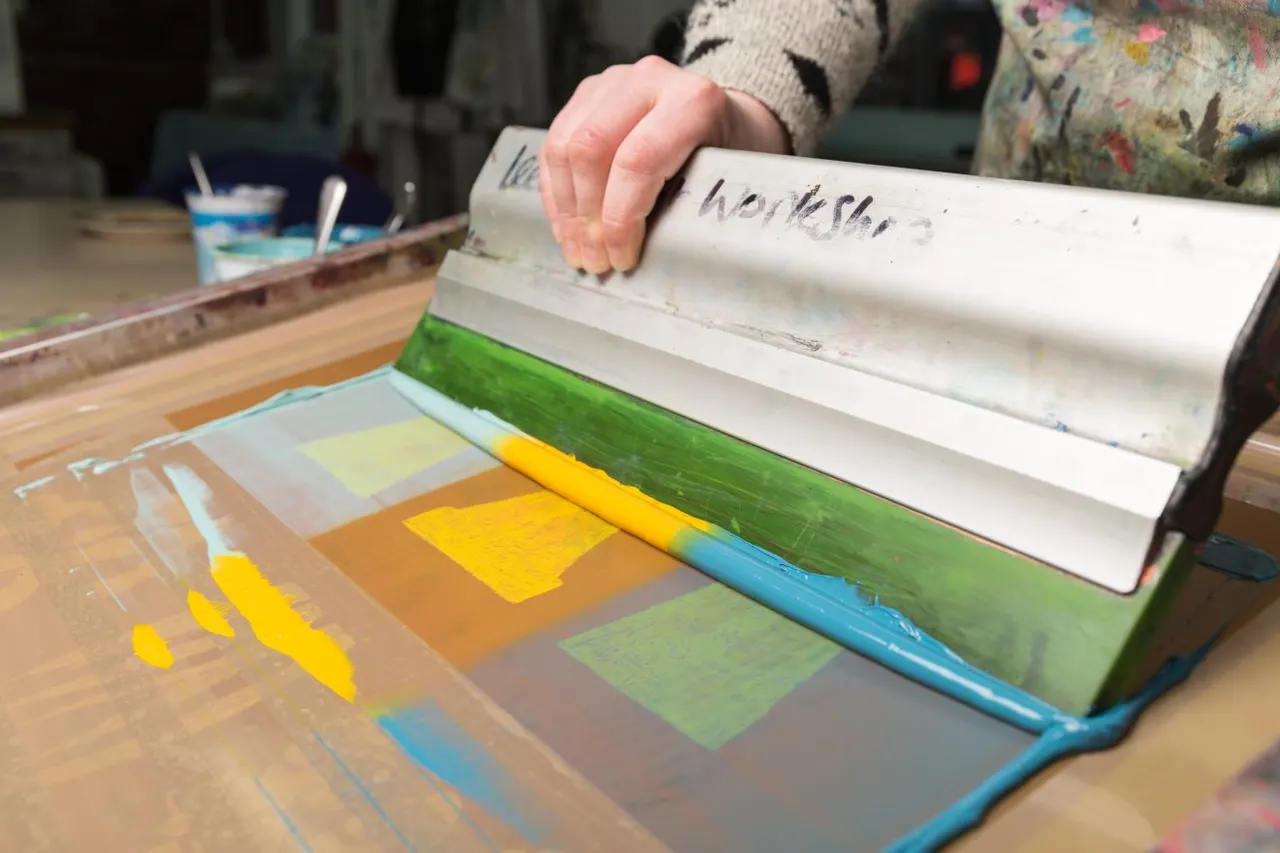 Child's hand rolling paint across a wooden printing block with colourful painted sections during an art workshop.