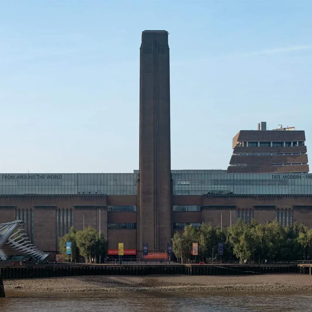 This is a photograph, not a designed graphic.

Art gallery building with tall brick chimney viewed from across the Thames on a clear day.
