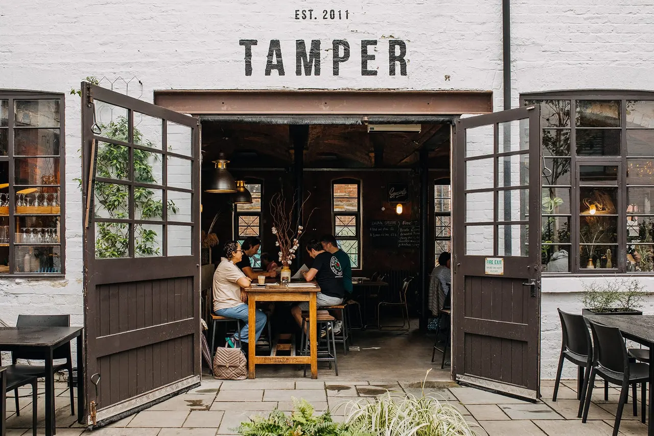 People sitting at tables inside a café with open double doors and white brick exterior.