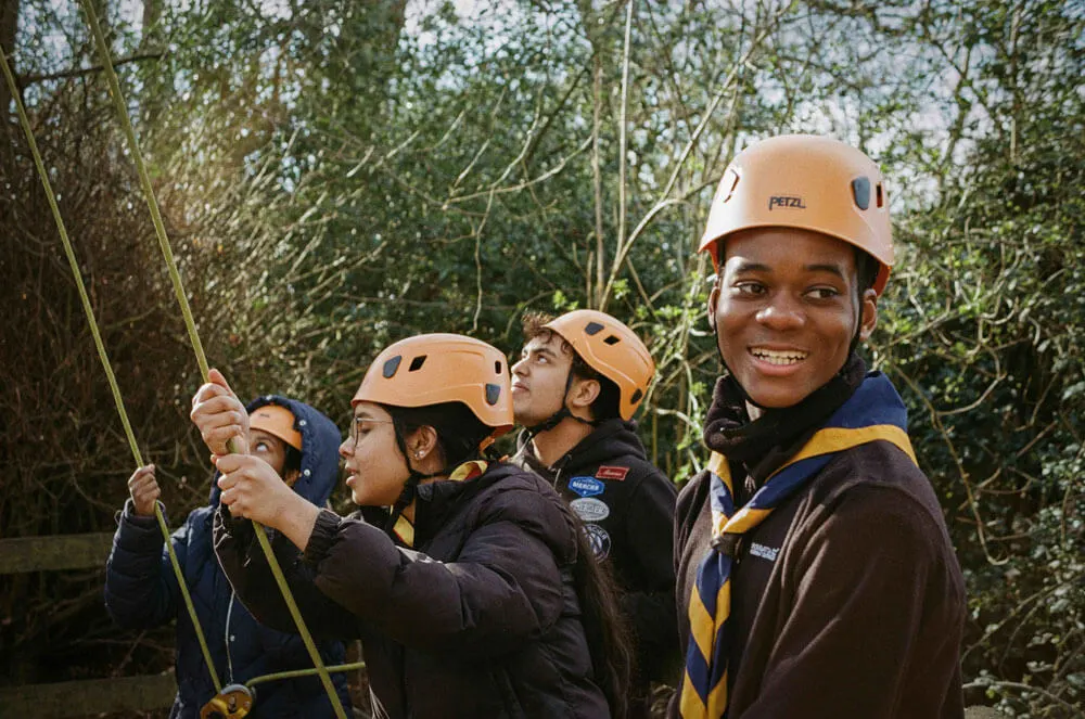 Group of four people wearing climbing helmets and harnesses on a rope activity in a wooded area.