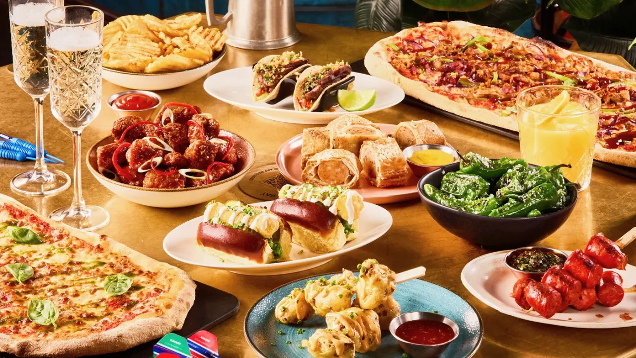 PHOTOGRAPH

Spread of food and drinks on a wooden table including pizza, tacos, meatballs, chips, and cocktails.