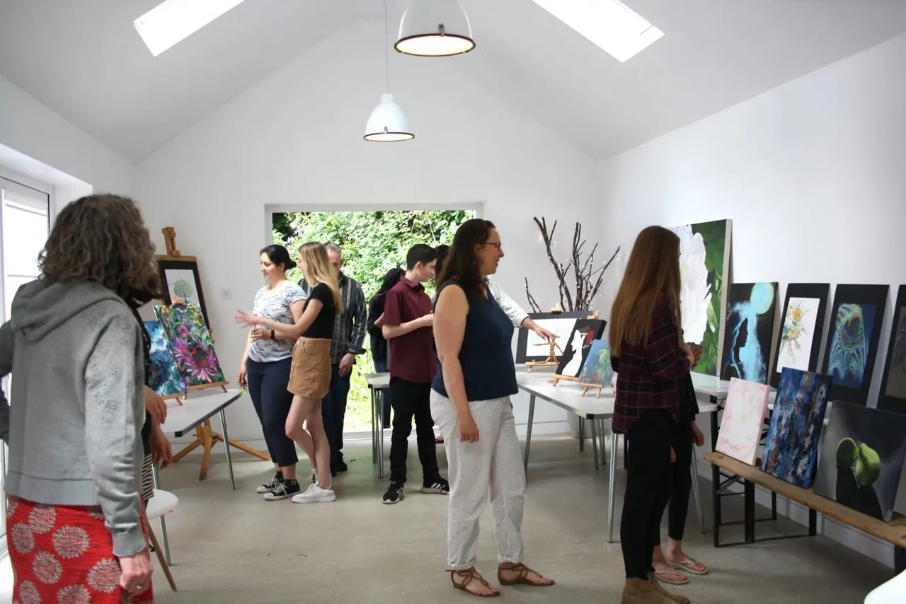 Group of visitors viewing artwork displayed on easels in a bright, modern gallery space with skylights.