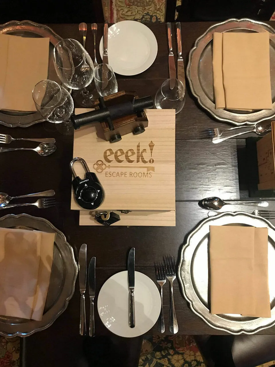 Overhead view of a formal dinner table set for four with plates, cutlery, glasses and napkins around a wooden puzzle box.