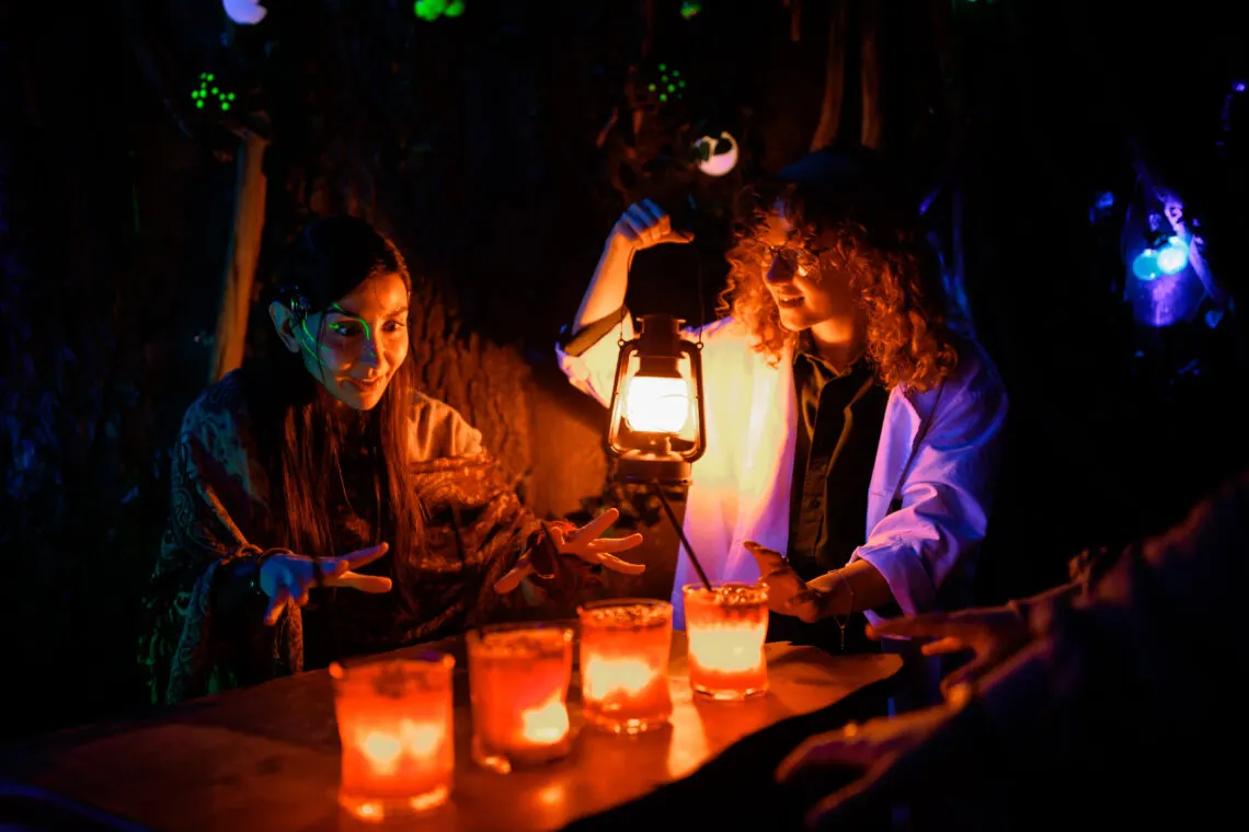 People gathered around a table with glowing lanterns and candles in a dimly lit venue with colourful ambient lighting.