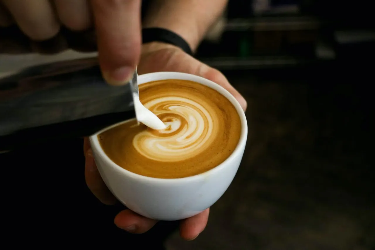 Barista pouring milk into coffee to create latte art in a white cup.