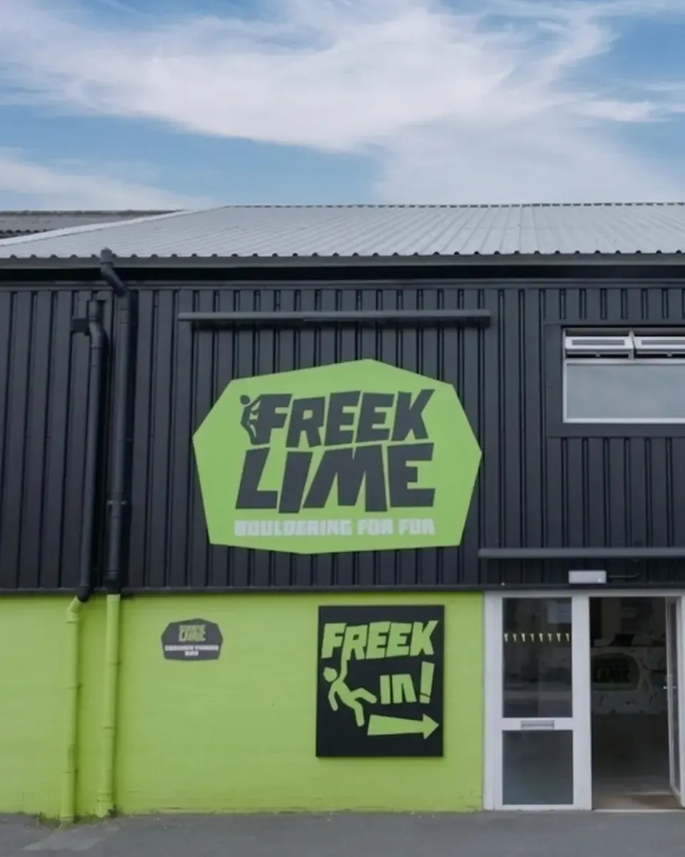 Modern single-storey leisure building with bright lime-green and dark grey corrugated metal facade, clear blue sky above.