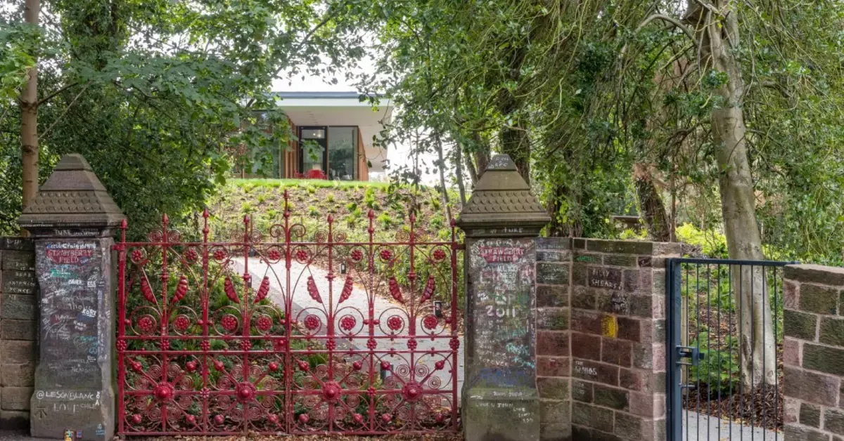 Red ornate gates with climbing ivy leading to a modern building surrounded by mature trees.