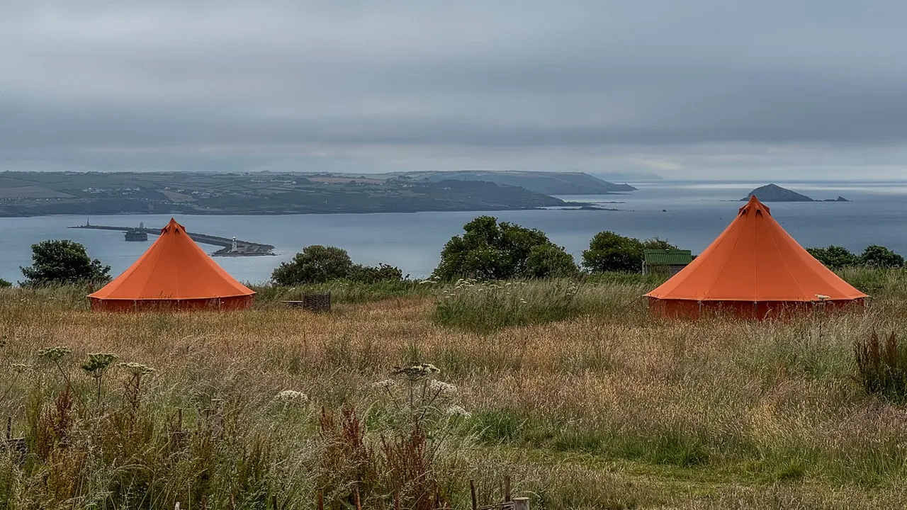 Two orange glamping tents in a grassy field overlooking a bay with islands and coastline.