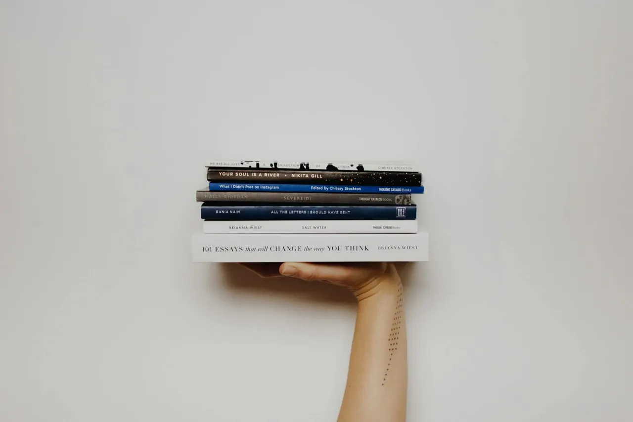 Person's arm holding a stack of books against a white wall.