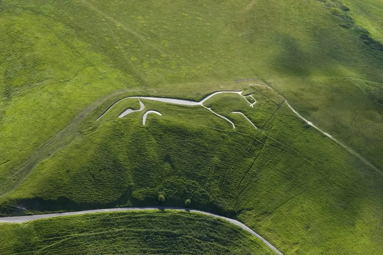 Aerial view of the Uffington White Horse chalk figure carved into a green hillside with surrounding landscape.