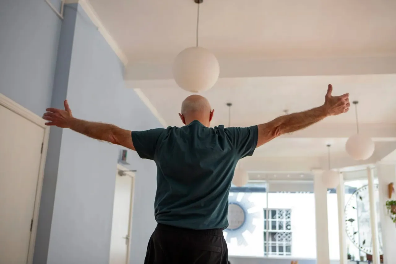 Man with arms outstretched in a bright, modern studio space with pendant lights.