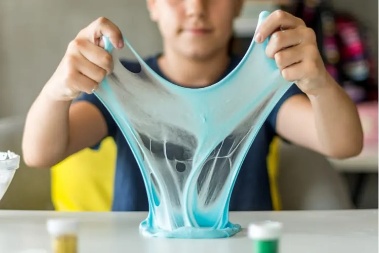 Child stretching blue slime between their hands at a table during a hands-on activity.