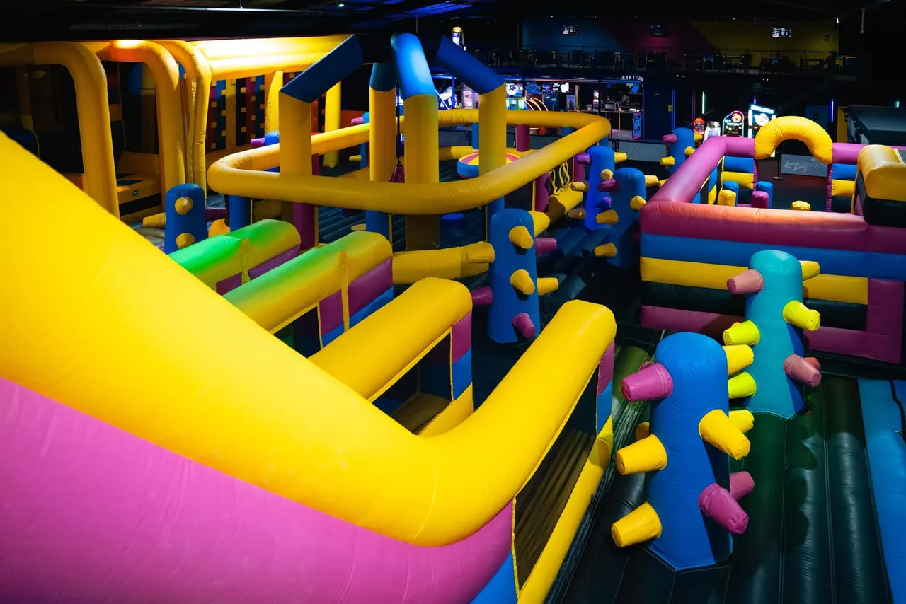 Colorful inflatable obstacle course with yellow, blue, pink and green padded structures for children to climb and navigate through.