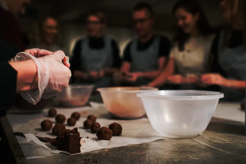 A person dusts chocolate truffles with cocoa powder whilst other participants watch a chocolate-making class.