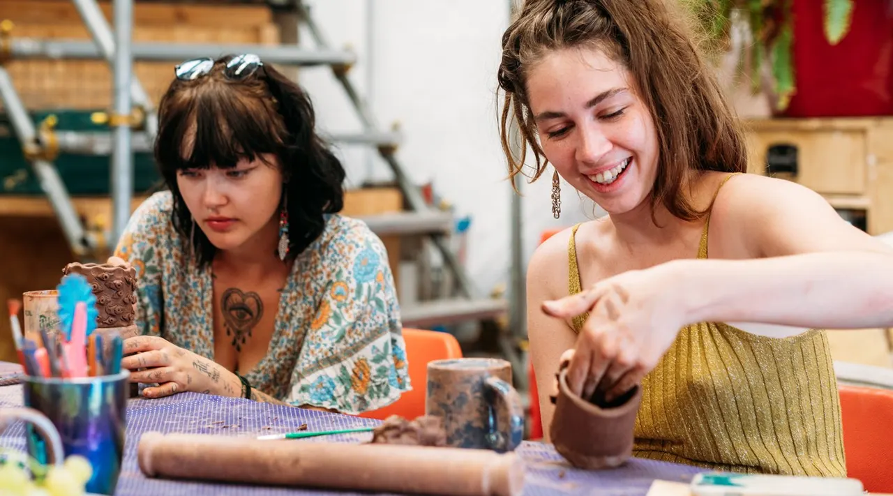 Two women working with clay at a pottery wheel and table in a studio workshop.