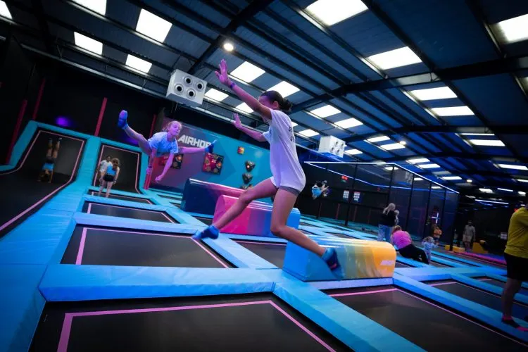 Child jumping on a trampoline at an indoor trampoline park with neon-lit blue and pink features.