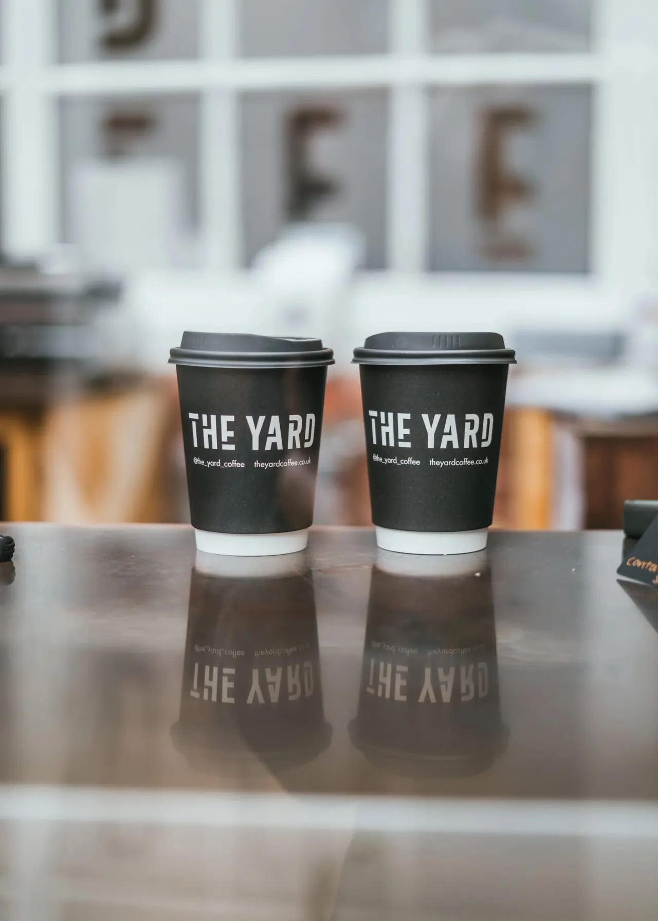 Two branded coffee cups sitting on a reflective counter inside a café.