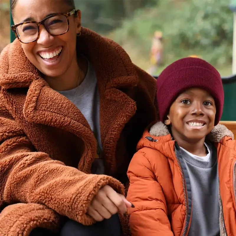 Woman and child smiling together outdoors wearing warm winter clothing at a leisure venue.