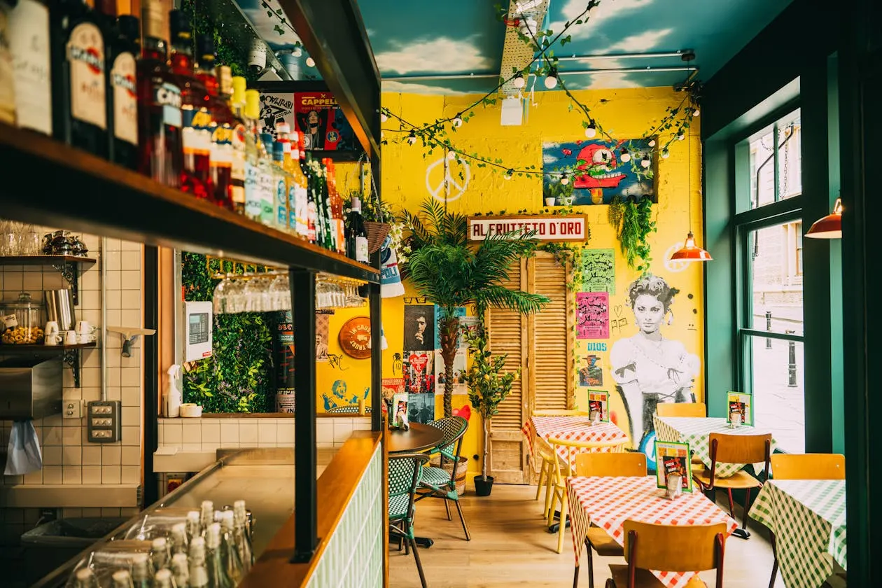 Colourful Italian pizzeria interior with bright yellow and green walls, hanging plants, checkered tablecloths, wooden chairs and vintage decor.