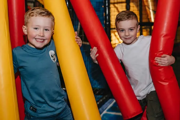 Two young children smiling among large colourful inflatable tubes at an indoor play facility.