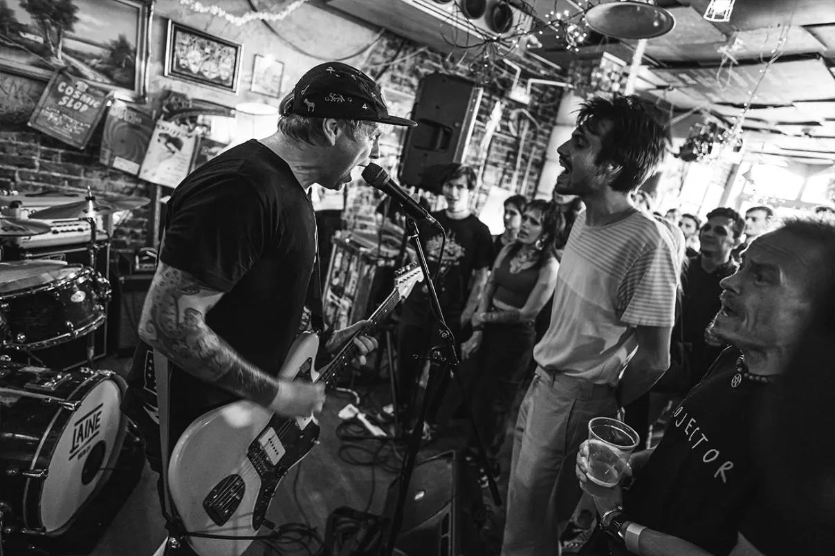 Live band performing in a crowded bar, with guitarist singing at microphone whilst audience watches in intimate venue.