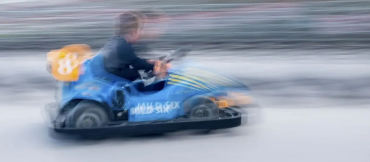 Person driving a blue bumper car at speed on a track.