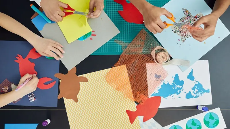 Children's hands creating colourful paper crafts and collages at a craft table.