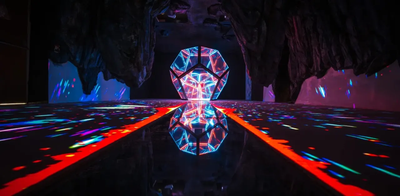 Immersive dark room with neon geometric light installation featuring glowing octagonal shapes and colourful beam patterns on the floor.